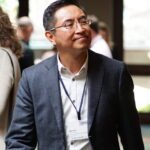Equity A middle-aged East Asian man wearing glasses and a dark blazer smiles slightly, wearing a name tag indicating his name is Bennett, his affiliation with Jacobs Center for Neighborhood Innovation and Qualcomm, and a lanyard, attending a conference or event.
